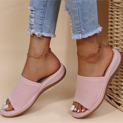 Slides in soft pale pink with a breathable knit strap, worn on feet beside wicker 4