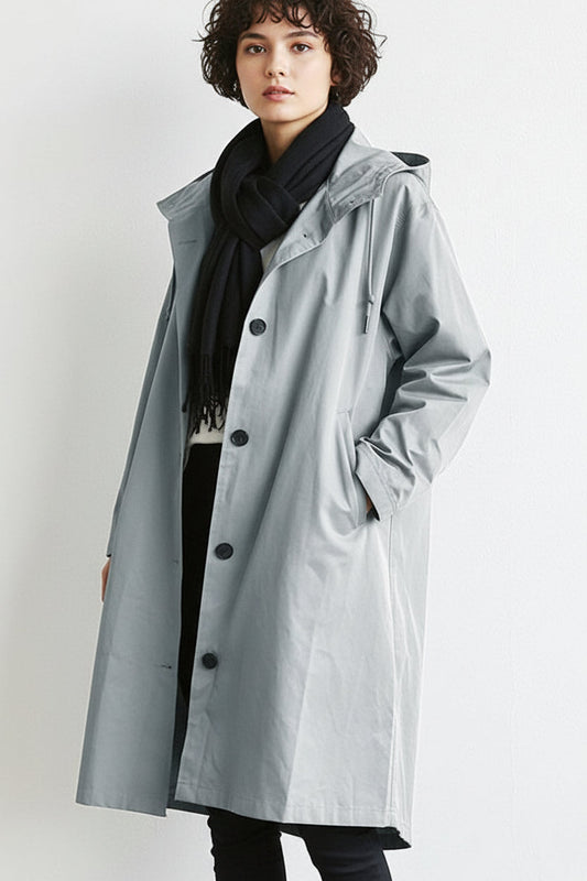Model in a pale grey hooded button-up coat with a black fringed scarf, hand in pocket 1