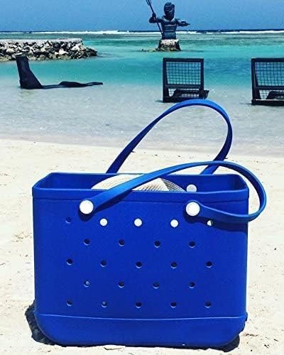 Bright blue tote standing on a sandy beach with the sea and a statue behind, handles looped over a hat. 23
