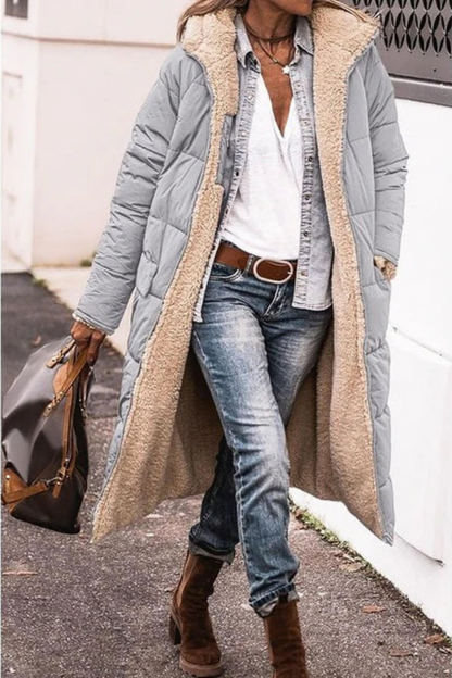 Model in a light grey quilted long coat with fleece-lined hood, carrying a handbag along a pavement 8