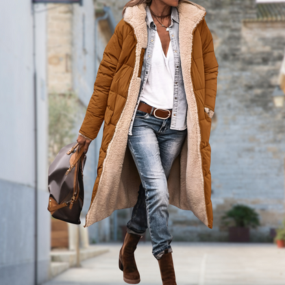 Model walking outdoors in a camel-brown quilted long coat, open to show cream fleece lining 9