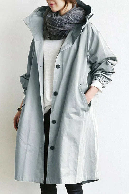Model wearing the longline hooded coat in pale grey, buttoned at the front, with a grey scarf and one hand in the pocket. 1