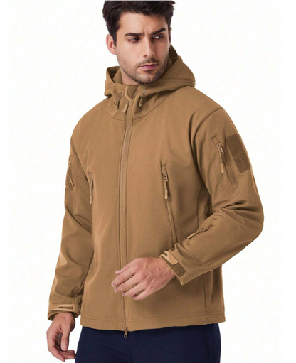 Model in the tan hooded jacket, turned slightly sideways, showing the full-length front zip, chest pockets and hook-and-loop sleeve patch. 16